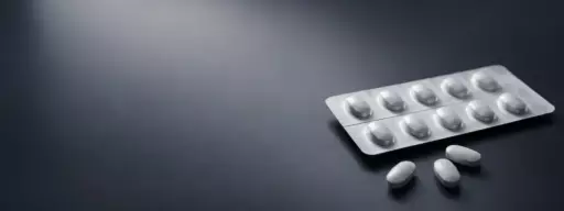 Blister packs with white tablets on a dark surface, a few pills scattered nearby.