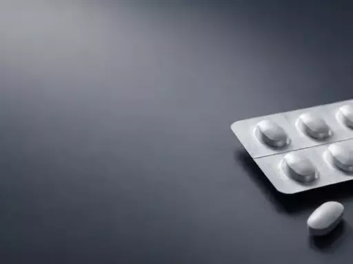 Blister packs with white tablets on a dark surface, a few pills scattered nearby.