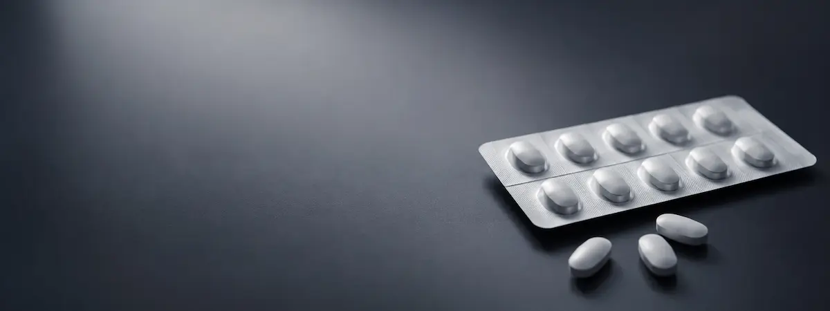 Blister packs with white tablets on a dark surface, a few pills scattered nearby.