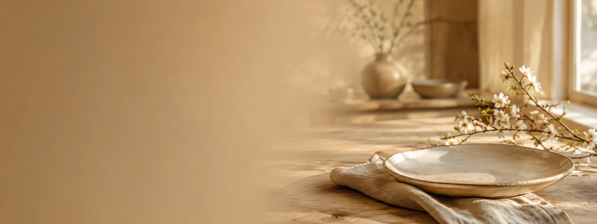 Sunny rustic table with a ceramic plate on a folded napkin, and a blossoming branch on a sunlit wooden surface.